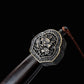 Gros plan sur le pommeau décoré d’une épée chinoise Jian Longquan, avec poignée sombre type ébène, garniture métallique ornementée, motif de dragon, cordon brun et fond noir.
