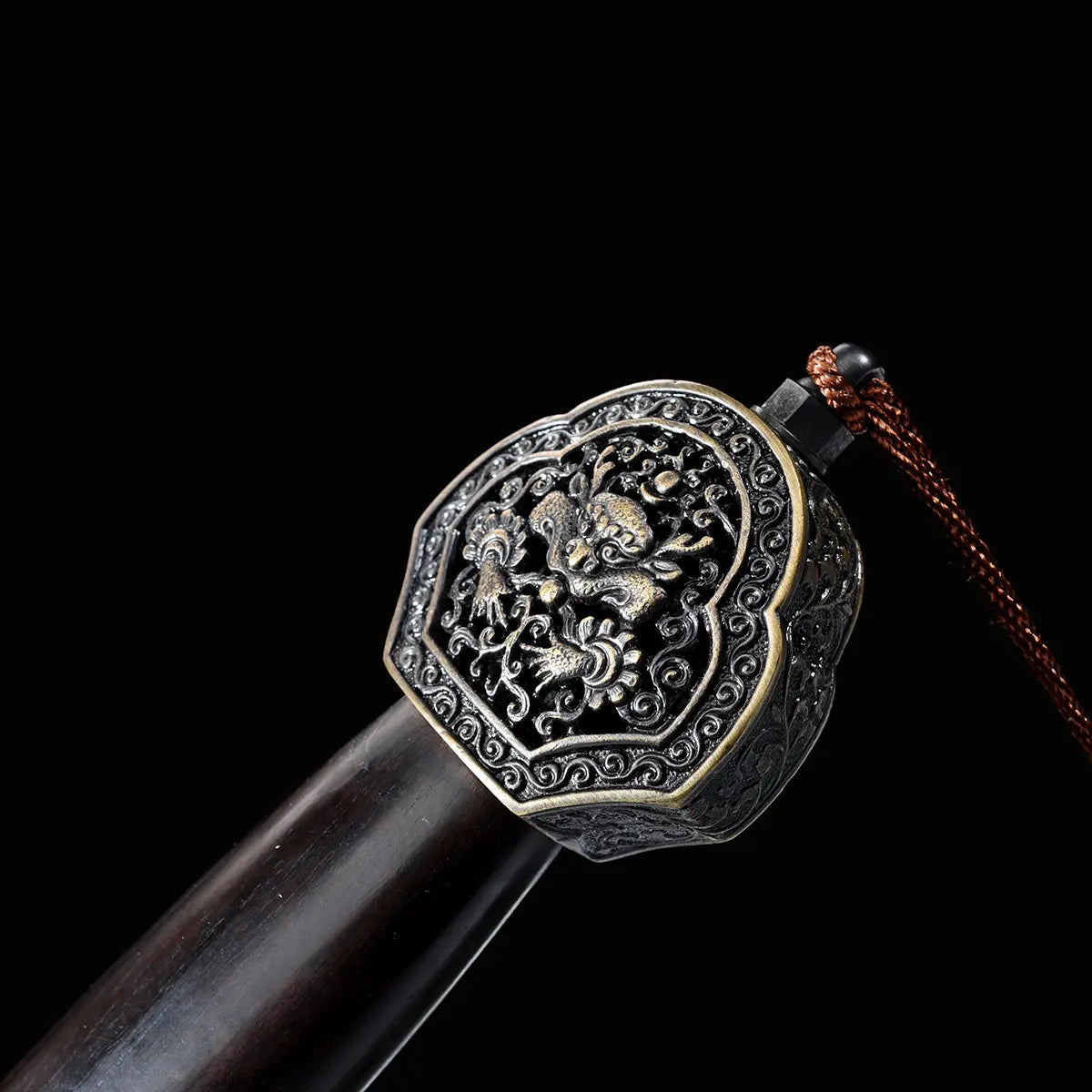 Gros plan sur le pommeau décoré d’une épée chinoise Jian Longquan, avec poignée sombre type ébène, garniture métallique ornementée, motif de dragon, cordon brun et fond noir.