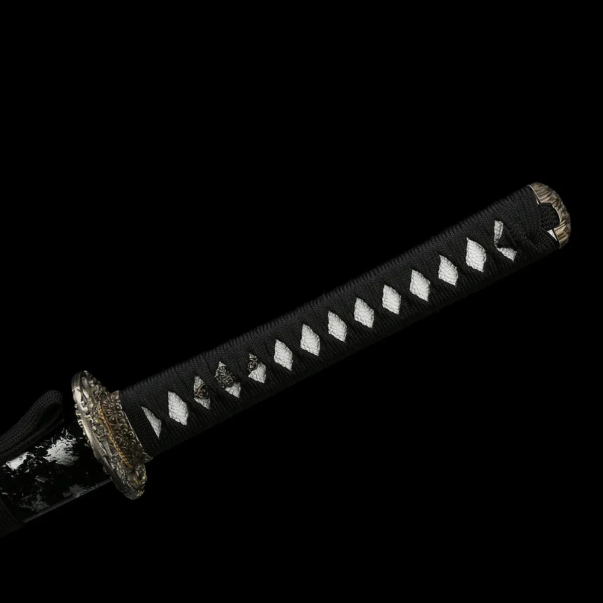Full view of the handle of the Japanese handmade katana Renge no Ken on a deep black background, black tsuka tightly wrapped with black cotton cord over white ray skin diamonds, lotus motif menuki visible under the wrap, dark metal lotus-pattern tsuba and kashira, katana shown partially sheathed with black glossy saya
