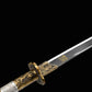 Sabre chinois Dao BAI LONG en gros plan sur fond noir, avec lame sombre partiellement visible, inscription dorée, gorge longitudinale, garde en laiton ornée et poignée blanche texturée avec détails métalliques décoratifs.