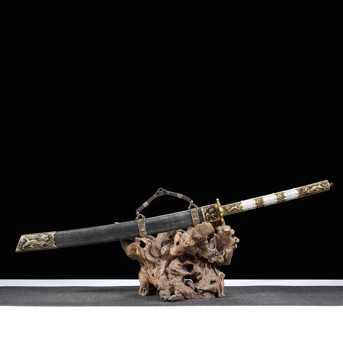Sabre chinois Dao BAI LONG présenté dans son fourreau sur un support en bois naturel, avec fond noir, poignée blanche texturée, garnitures en laiton doré, chaîne décorative et fourreau sombre orné de détails métalliques.