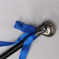 Gros plan de la poignée de la canne-épée “Blue Noble Cane”, tête sculptée en forme de crâne métallique argenté avec détails gravés, entourée d’un ruban bleu vif. La canne est posée sur un fond gris clair texturé, mettant en valeur le contraste entre le métal poli, le tissu et le tube acier laqué noir.