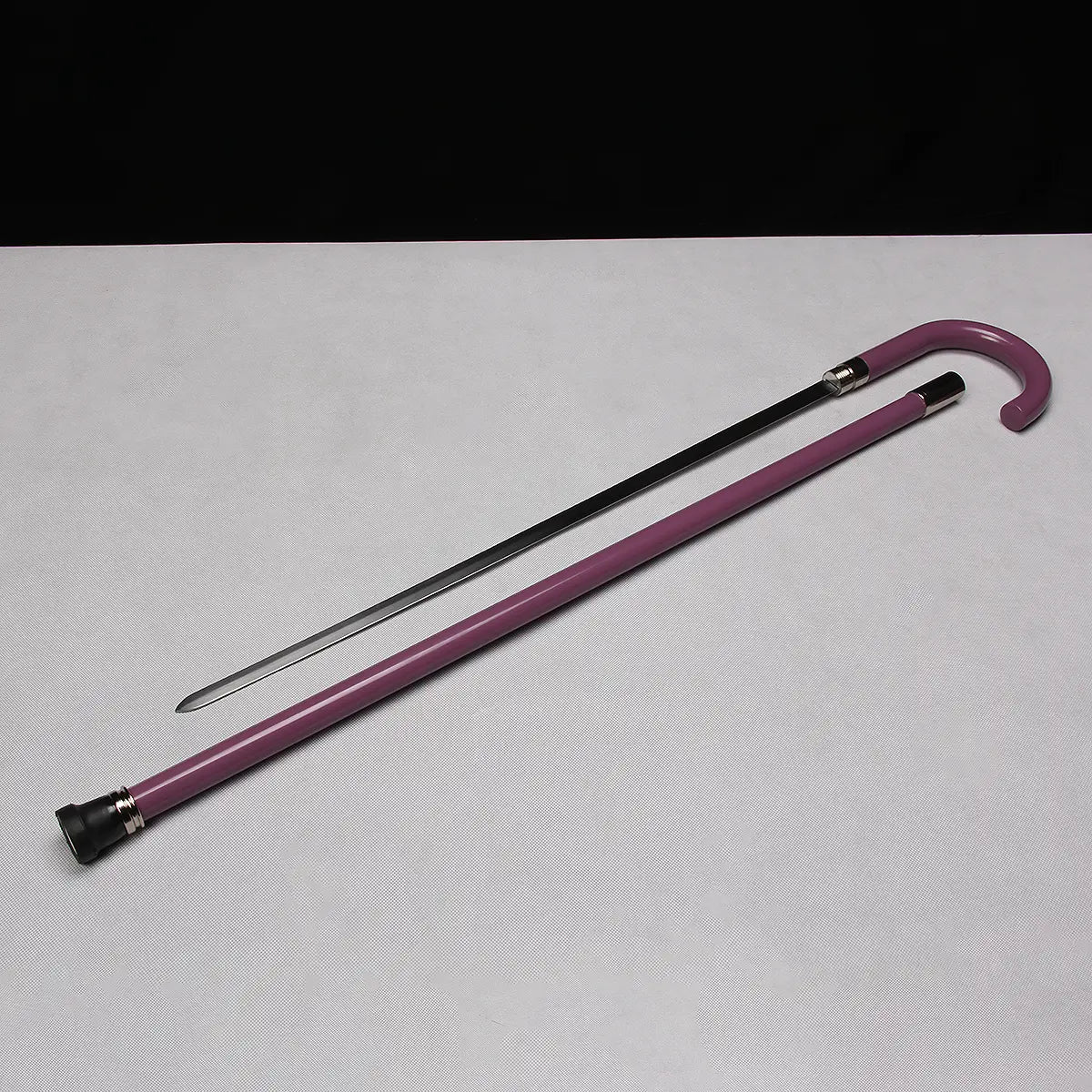 Canne-épée “Purple Symphony” présentée dégainée sur un fond gris clair contrastant avec un arrière-plan noir ; la lame inox polie est entièrement sortie du tube en acier laqué violet, avec la poignée en crochet et les bagues métalliques bien visibles, éclairage studio soulignant les reflets du métal et la brillance du fourreau.