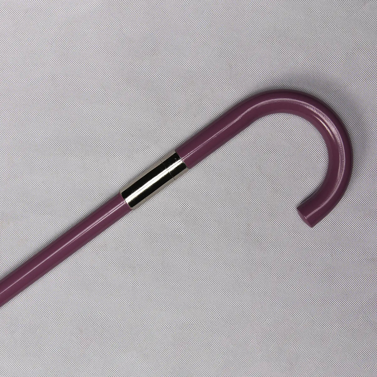 Gros plan de la poignée en crochet de la canne-épée “Purple Symphony”, tube en acier laqué violet posé sur un fond gris clair texturé, avec une bague métallique chromée bien visible à la jonction ; éclairage homogène révélant la brillance de la laque et les reflets du métal.
