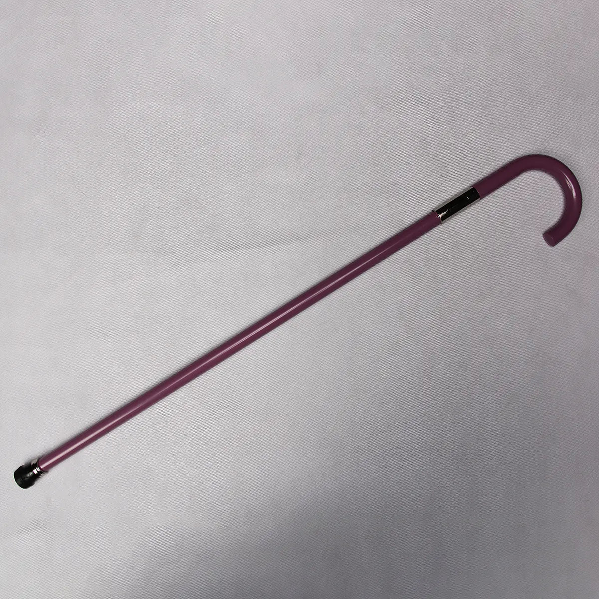 Canne-épée cosplay “Soul King” posée à plat sur un fond gris clair texturé, tube en acier laqué violet visible sur toute la longueur, poignée en crochet et bague métallique chromée près de la jonction, embout caoutchouc noir en bas, éclairage diffus révélant la brillance de la laque.