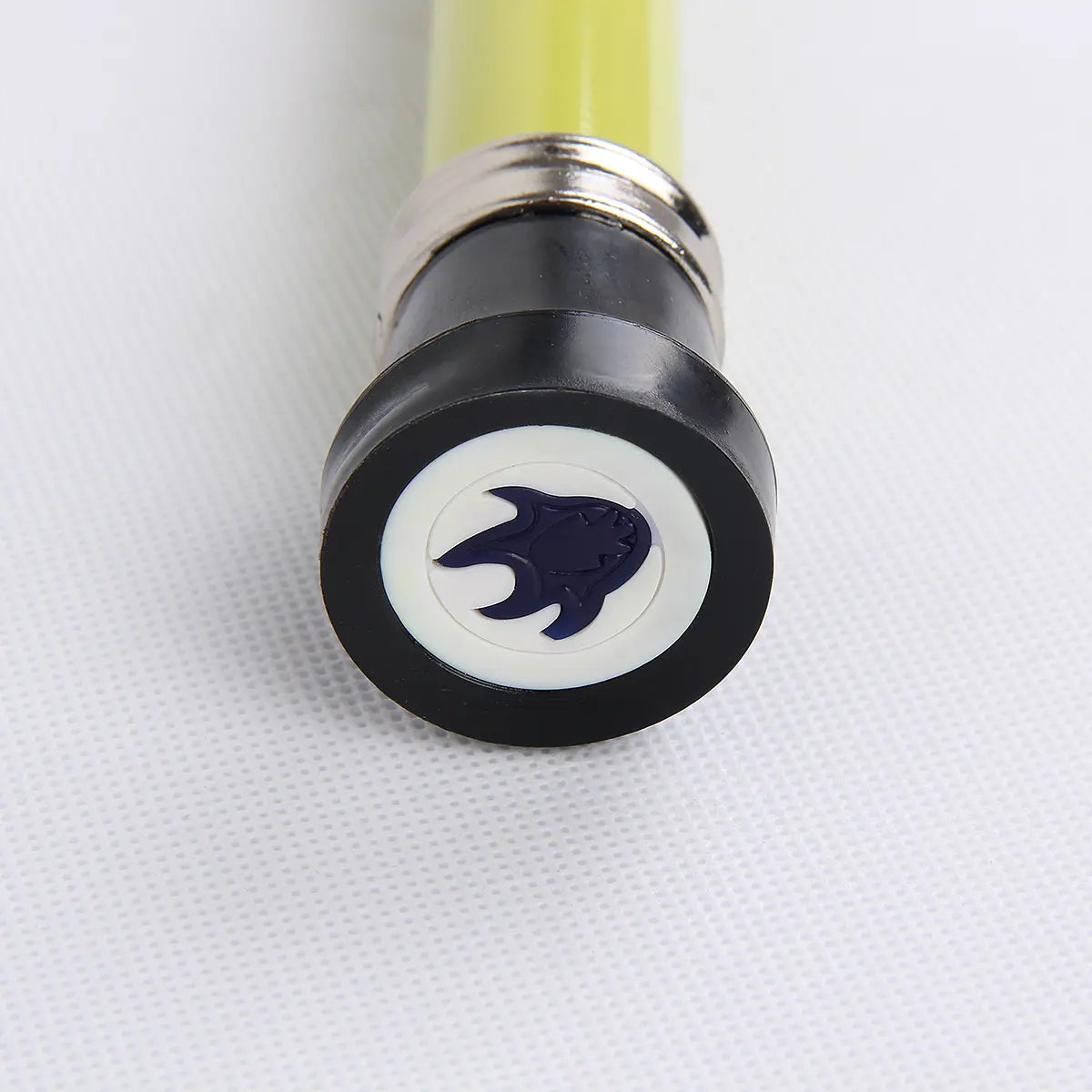 Gros plan sur l’embout en caoutchouc noir de la canne-épée Urahara Bleach, avec logo bleu incrusté en bout ; tube laqué jaune flouté en arrière ; photo réalisée sur fond blanc texturé.