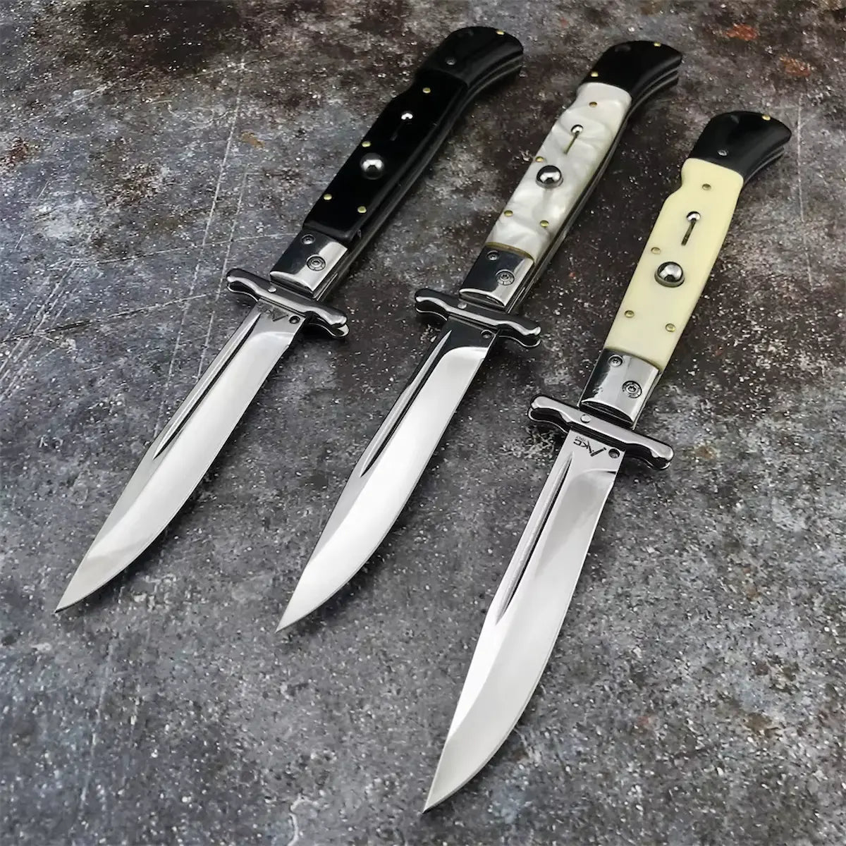 trois couteaux automatiques italiens « Original Mafia » disposés sur fond pierre gris texturé, lames en acier 440C miroir orientées vers l’avant, manches noir, nacré et blanc ivoire contrastés, composition brute et élégante dans l’esprit vintage Blade Bushido