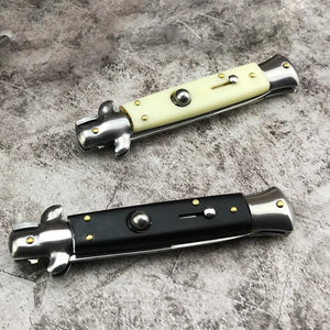 Deux couteaux automatiques italiens Stiletto repliés posés sur un fond à texture pierre grise. L’un présente un manche noir brillant, l’autre un manche ivoire clair, chacun avec des rivets dorés et des finitions métalliques chromées. L’ambiance met en avant le contraste entre tradition italienne et élégance moderne – Blade Bushido.
