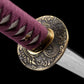 Close-up detail of the handcrafted Japanese katana Dokuryu on a black background, focusing on the round metal tsuba engraved with a Japanese dragon surrounded by traditional cloud motifs, brass habaki fitted at the base of the blade, purple tsuka wrap in tight traditional braid revealing white ray skin panels beneath, blade partially visible, minimalist studio composition with no scabbard and no stand.
