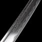 Macro close-up of the folded steel blade of the handcrafted Japanese katana Dokuryu on a black background, showing detailed layered grain patterns along the blade surface with natural flowing lines, subtle contrast between hardened edge and softer steel body, polished finish reflecting light, no scabbard or fittings visible, minimalist studio composition focused on steel texture.
