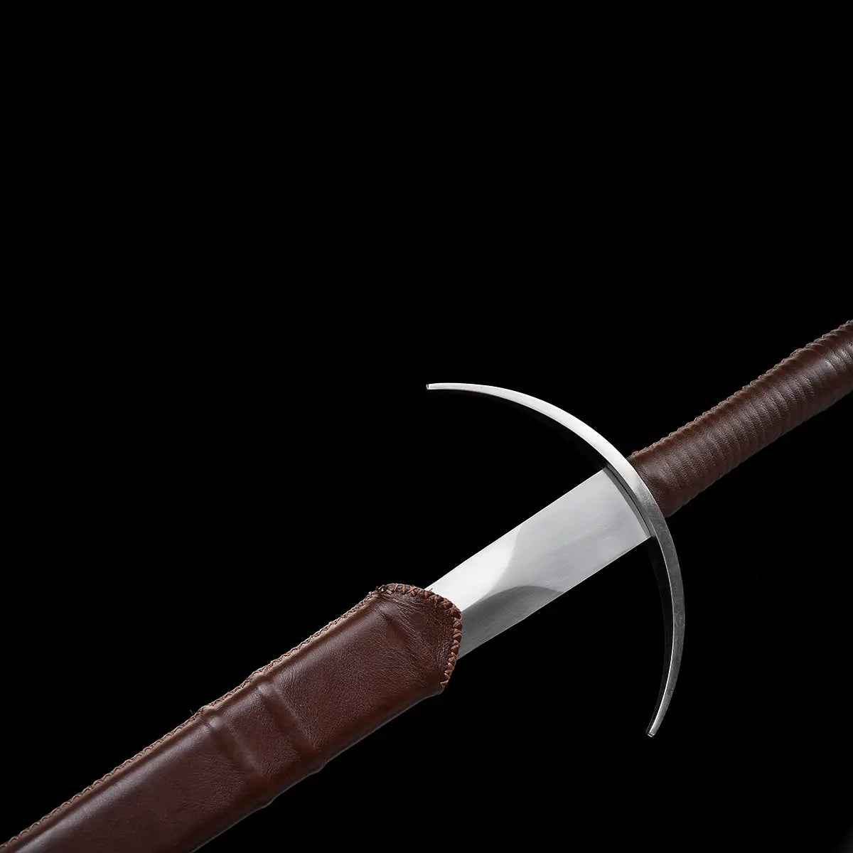 Gros plan de l’épée longue Aegis Terra en train d’être dégainée de son fourreau brun, montrant la garde en croix courbée, la lame en acier 1060 polie et les coutures du cuir. Fond noir minimaliste mettant en valeur les détails médiévaux, la finition artisanale et la qualité du fourreau.