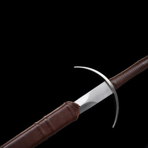 Gros plan de l’épée longue Aegis Terra en train d’être dégainée de son fourreau brun, montrant la garde en croix courbée, la lame en acier 1060 polie et les coutures du cuir. Fond noir minimaliste mettant en valeur les détails médiévaux, la finition artisanale et la qualité du fourreau.