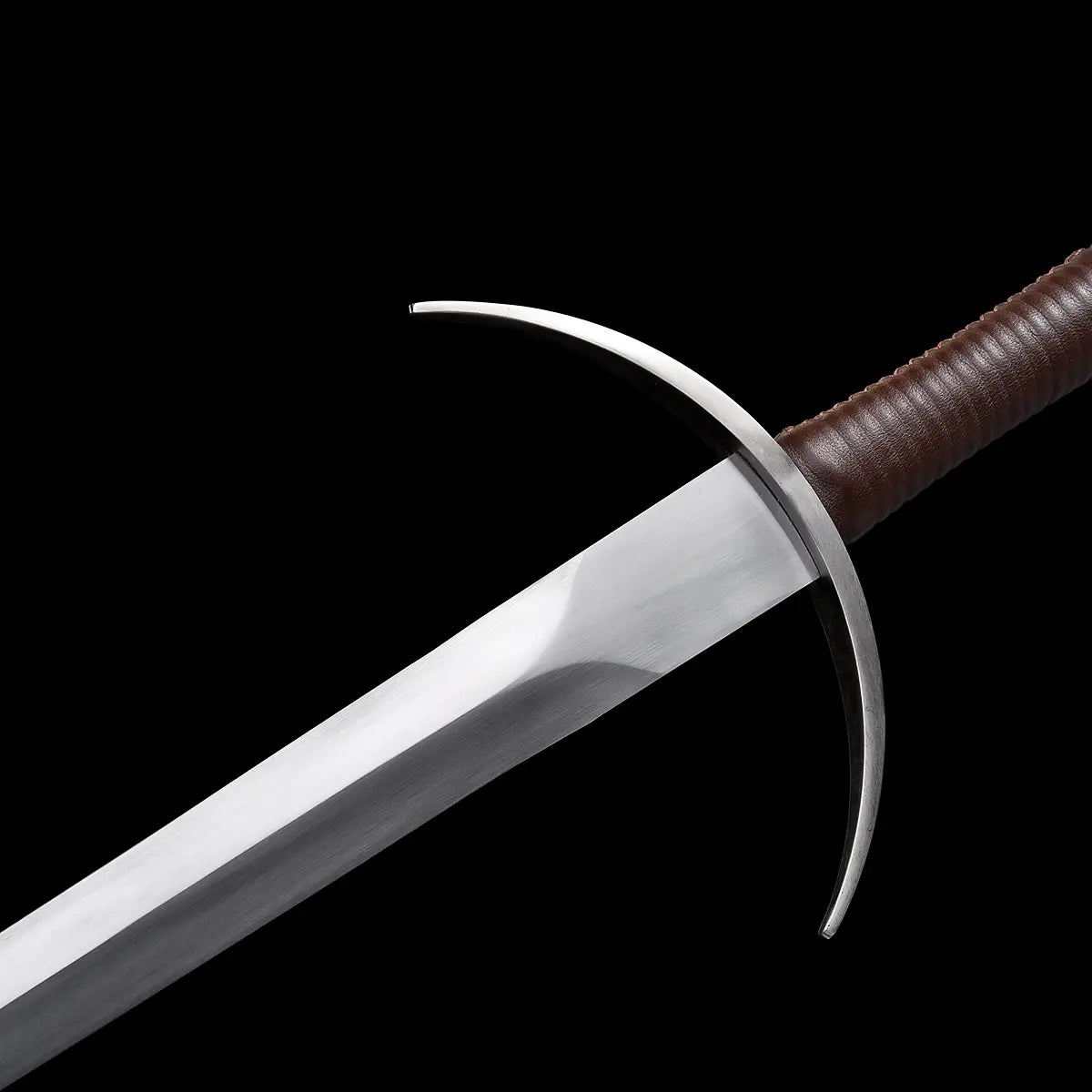 Gros plan sur la garde en croix courbée de l’épée longue médiévale Aegis Terra, montrant les quillons incurvés en acier, la lame 1060 polie et la poignée gainée de cuir brun, sur fond noir uniforme. Image détaillée idéale pour mettre en valeur la construction, la protection de la main et l’esthétique médiévale de la longsword.