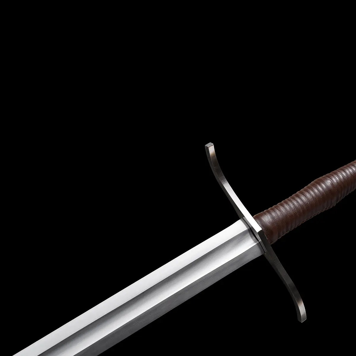 Gros plan sur la garde en croix de l’épée longue “Brune-Lame”, lame en acier 1060 avec gouttière visible, poignée gainée de cuir brun et quillons métalliques courbés, photographiée sur fond noir pour mettre en valeur les détails médiévaux et la finition premium Blade Bushido.