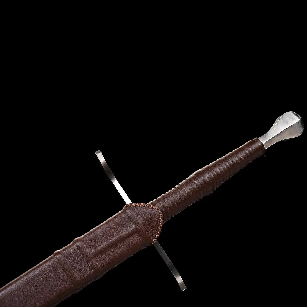 Gros plan sur la poignée de l’épée longue “Brune-Lame”, gainée de cuir brun, avec son pommeau métallique évasé et la garde en croix visible, le tout partiellement inséré dans le fourreau en cuir brun ; photographie sur fond noir mettant en valeur les matériaux et les finitions médiévales premium Blade Bushido.