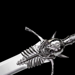 Détail de la garde de l’épée longue Dante Devil May Cry Rebellion photographiée sur fond noir uniforme, vue en léger angle de profil. Le crâne central sculpté en métal argen
