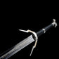 Vue rapprochée de la garde et du départ de la lame de l’épée longue Geralt de Riv The Witcher 3 sur fond noir uniforme, lame droite en acier poli avec inscriptions décoratives dorées visibles sur le plat, garde en croix anguleuse en métal argenté avec quillons asymétriques gravés, poignée longue gainée de cuir noir en enroulement serré, pommeau métallique partiellement visible, rendu fidèle à l’esthétique fantasy médiévale pour cosplay, collection et observation AMHE ou HEMA décorative
