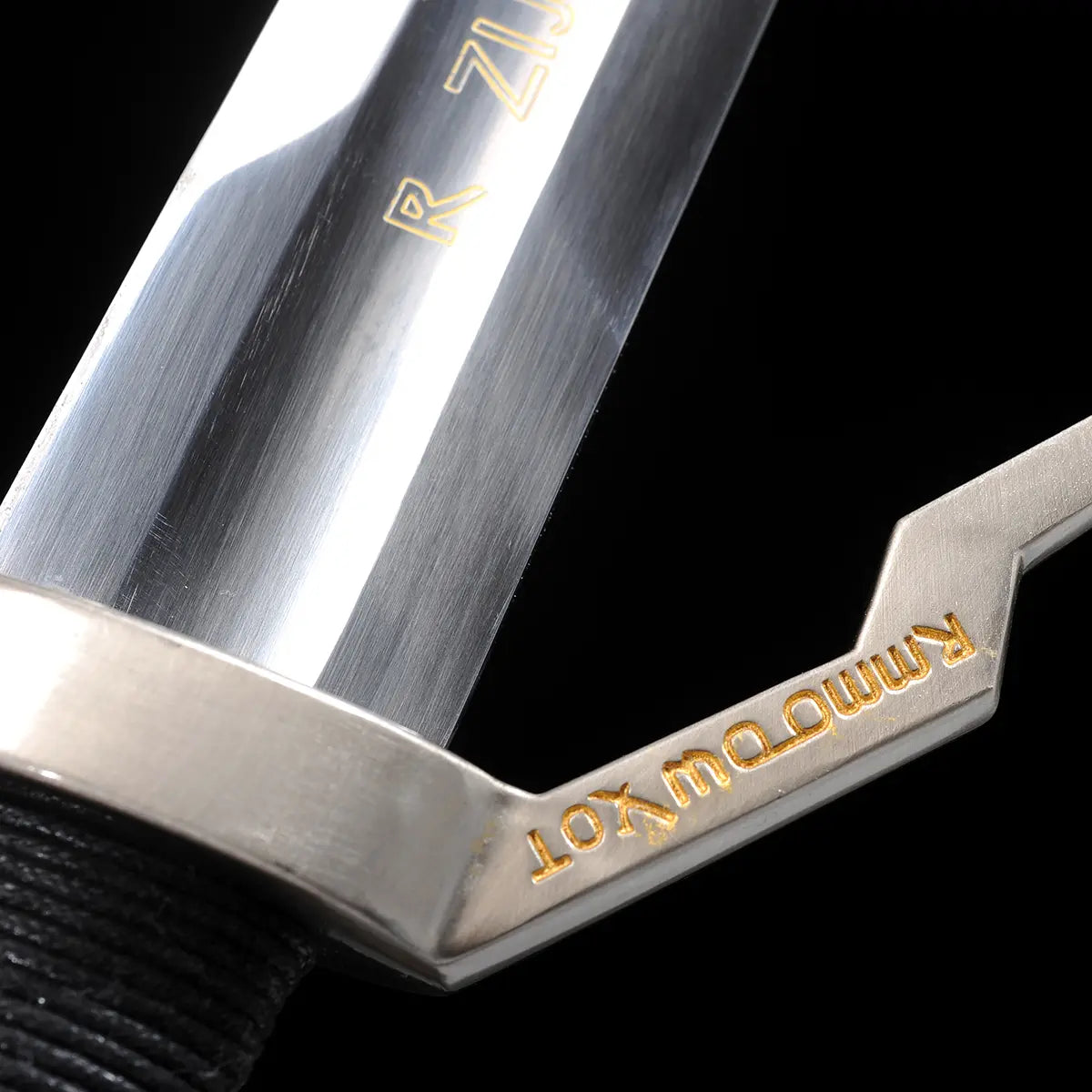 Gros plan sur la garde de l’épée longue Geralt de Riv The Witcher 3 sur fond noir uniforme, base de la lame en acier poli avec reflets longitudinaux, garde en croix anguleuse en métal argenté, quillon droit gravé d’inscriptions décoratives dorées, jonction nette entre la lame et la garde, poignée gainée de cuir noir visible en arrière-plan, vue détaillée destinée au cosplay, à la collection et à une observation
