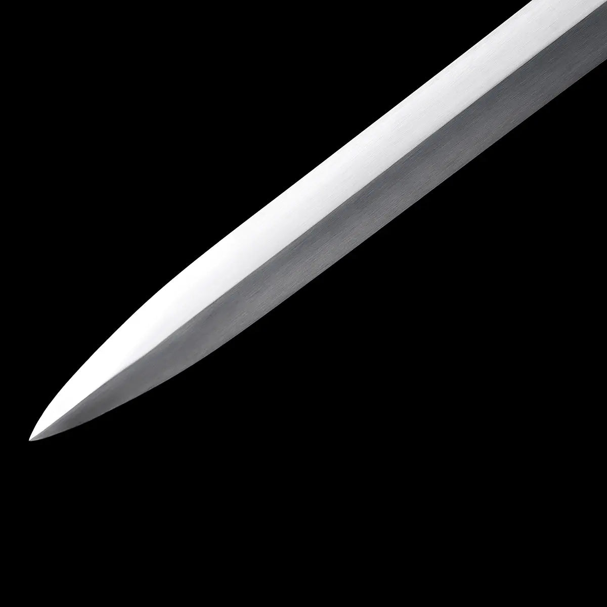 Gros plan sur la pointe de l’épée longue médiévale Crux Bellator, lame en acier carbone 1060 au polissage satiné, photographiée sur fond noir uniforme, montrant le tranchant, les reflets métalliques et la géométrie droite de la longsword.