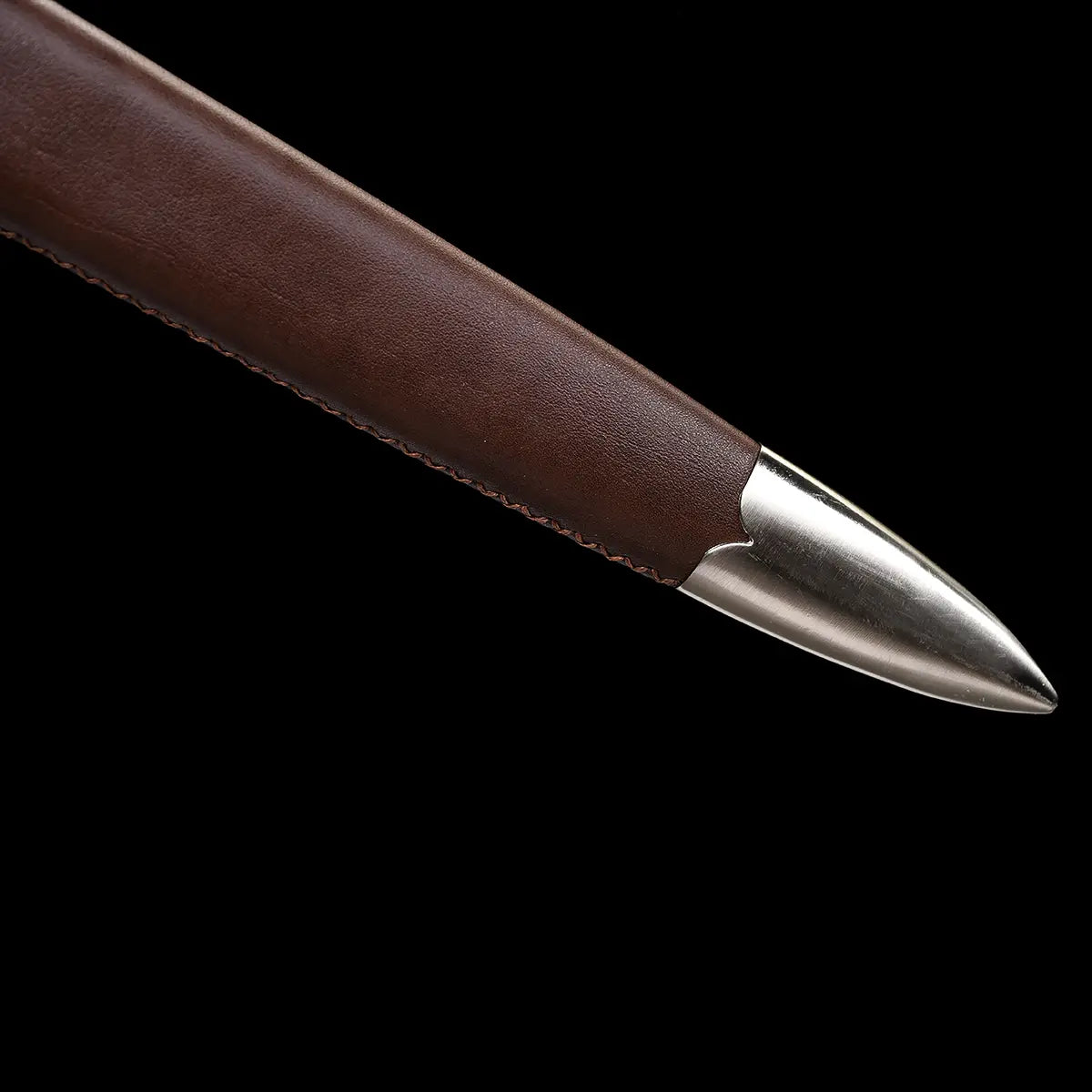 Gros plan du bout métallique renforcé du fourreau de l’épée longue médiévale Castelar, en cuir brun lisse avec couture latérale visible, présenté sur fond noir pour mettre en valeur la texture du cuir, la pointe en acier poli et les finitions artisanales du fourreau.