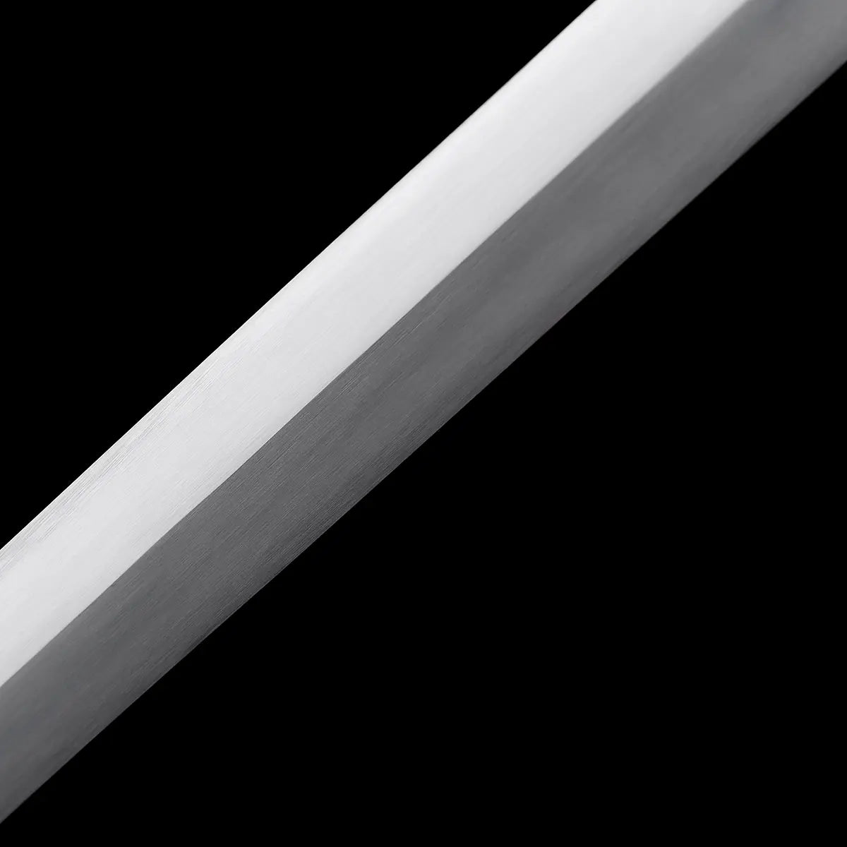 Détail de la lame de l’épée longue médiévale Corvus, acier carbone 1060 avec finition satinée brossée, arêtes nettes et géométrie droite, surface homogène sans gravure, photographiée sur fond noir profond pour souligner la pureté de la ligne et la rigueur de la forge médiévale.