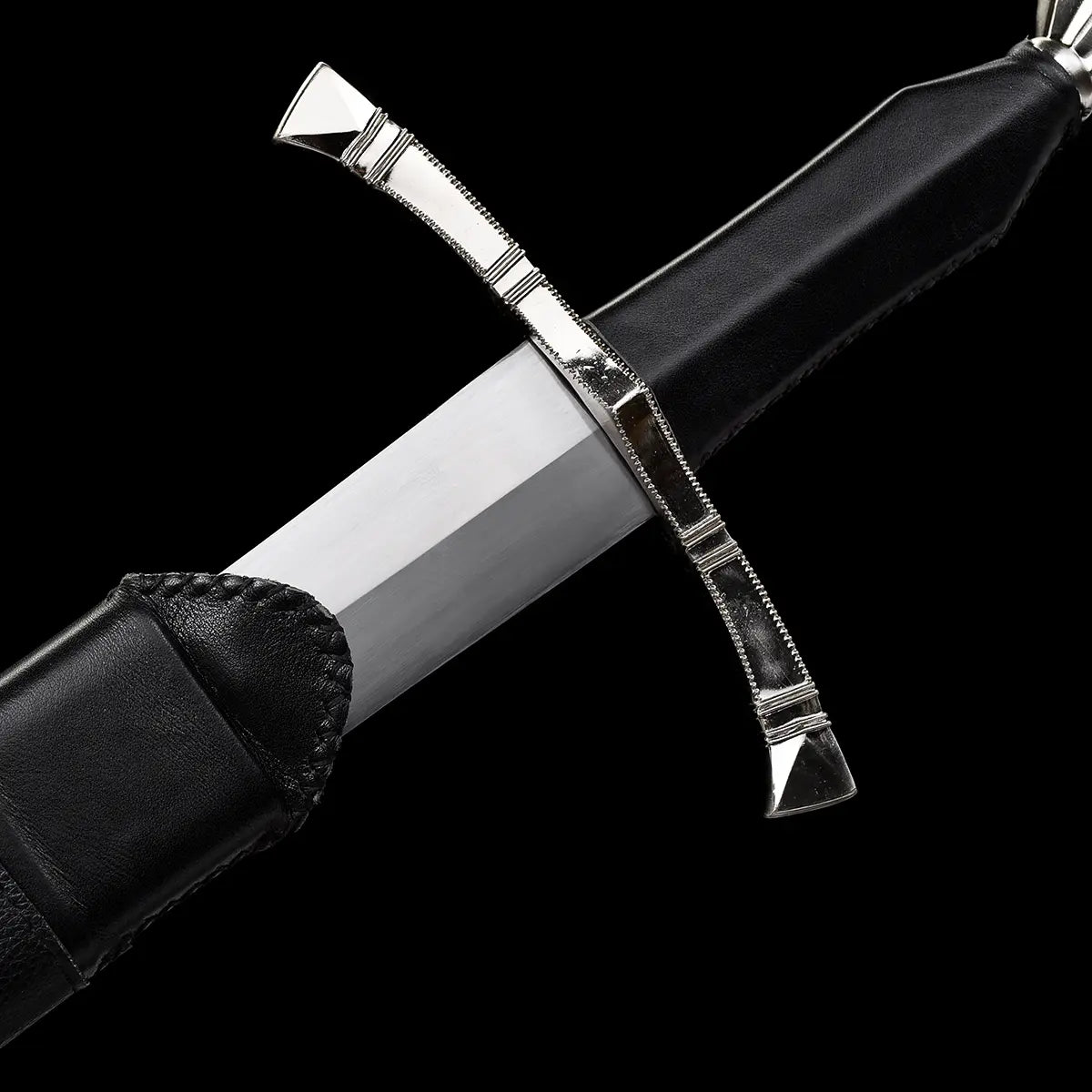 Gros plan sur la zone de sortie de lame de l’épée longue médiévale Corvus, lame droite en acier carbone 1060 finition satinée émergeant du fourreau en cuir noir, garde en croix à quillons droits en métal poli protégeant la main, poignée gainée de cuir sombre, photographiée sur fond noir profond pour une ambiance martiale, sobre et authentique.
