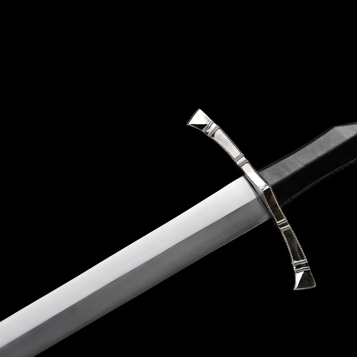 Détail de la garde en croix de l’épée longue médiévale Corvus, quillons droits en métal poli protégeant la main, jonction nette avec la lame droite en acier carbone 1060 finition satinée, poignée gainée de cuir sombre visible en arrière-plan, photographie sur fond noir profond créant une ambiance martiale et épurée.