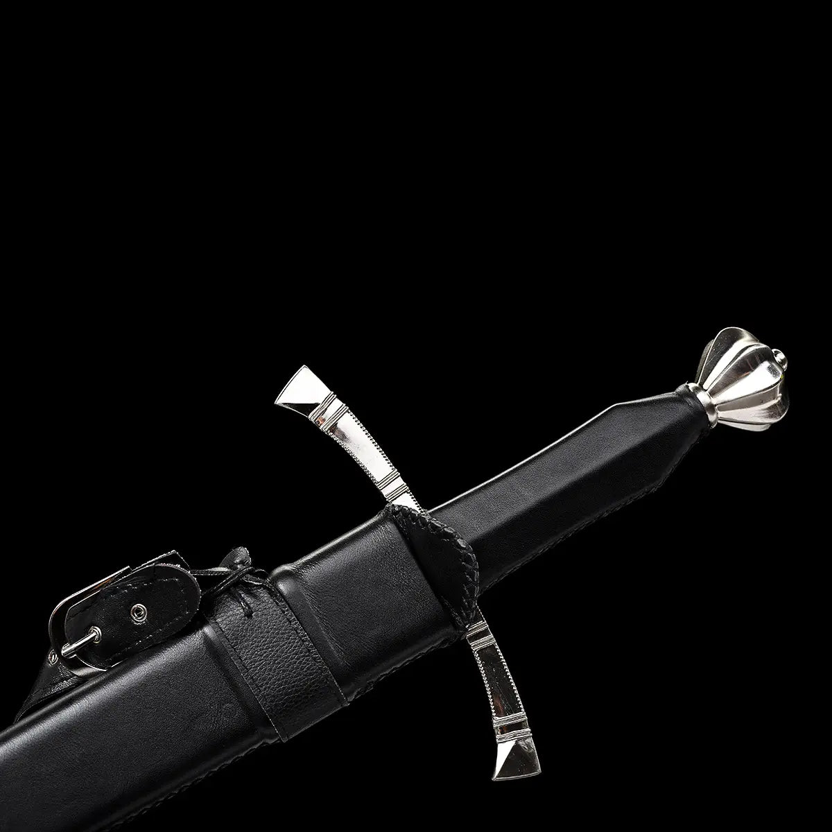 Détail de la poignée de l’épée longue médiévale Corvus, poignée en bois gainée de cuir noir cousu main, pommeau évasé type poire en métal poli assurant l’équilibre, garde en croix à quillons droits visible, fourreau cuir noir avec lanières de port en arrière-plan, photographié sur fond noir profond pour une ambiance sobre, martiale et haut de gamme.