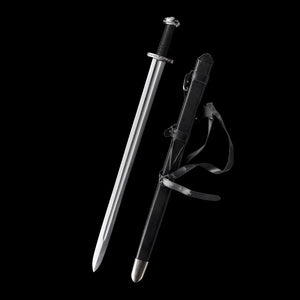 Épée longue médiévale Ravenna dégainée, présentée aux côtés de son fourreau en cuir noir, sur fond noir profond. Lame droite en acier 1060 polie, avec gouttière centrale, garde en croix métallique et pommeau évasé. Poignée gainée cuir noir offrant une prise ferme, idéale pour la pratique AMHE / HEMA, la coupe légère ou la collection médiévale.