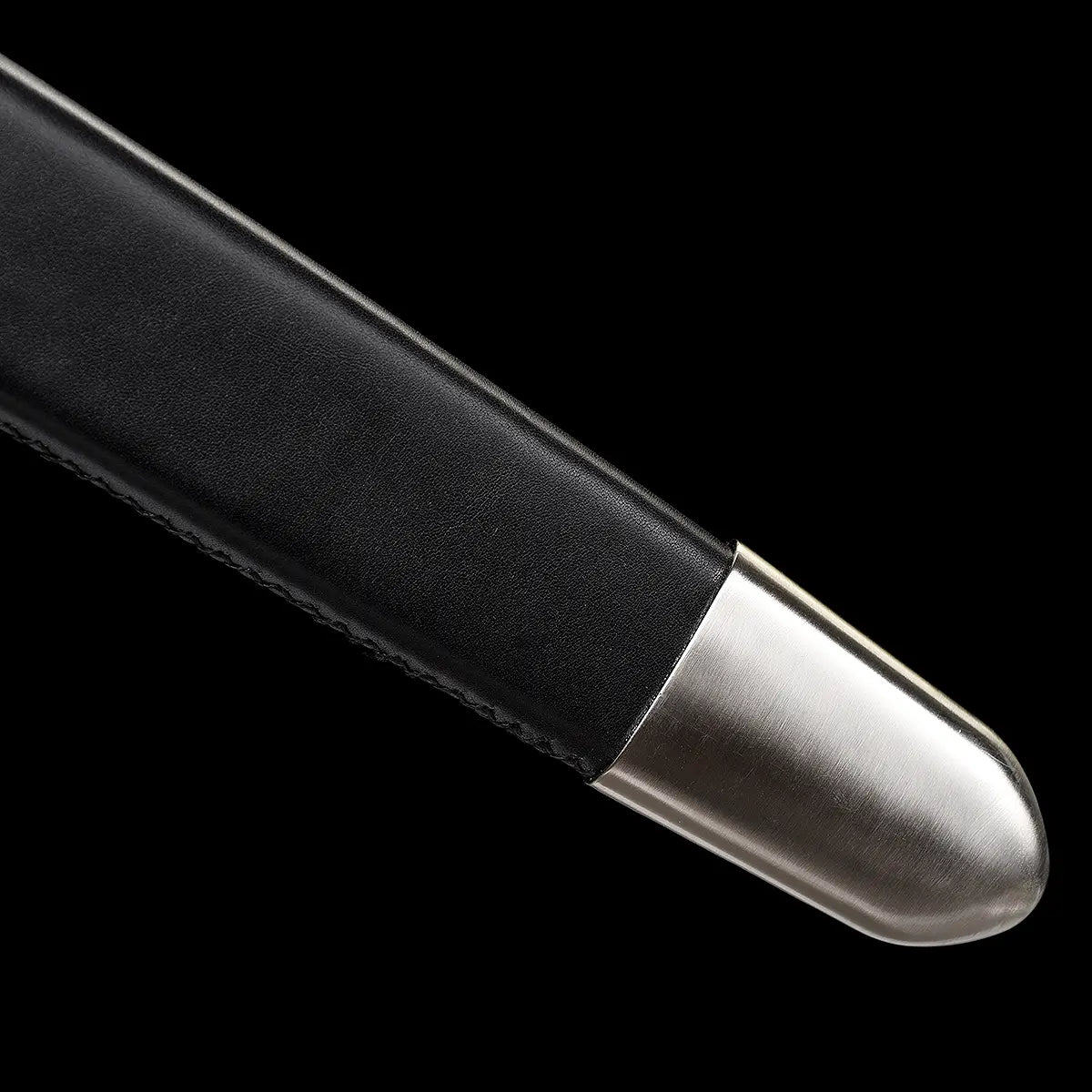 Gros plan sur l’extrémité du fourreau de l’épée longue médiévale Ravenna, photographiée sur fond noir uniforme. Fourreau en bois gainé de cuir noir, terminé par une bouterolle métallique argentée protégeant la pointe de la lame. Finition robuste et fonctionnelle, pensée pour le transport sécurisé, la pratique AMHE / HEMA ou la présentation en collection médiévale.