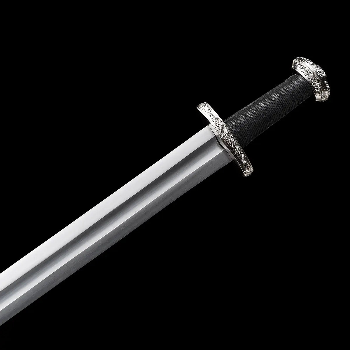 Vue détaillée de la poignée et de la garde de l’épée longue médiévale Ravenna sur fond noir uniforme. Poignée longue gainée de cuir noir offrant une prise main-et-demi stable, garde en croix courte en métal argenté et pommeau évasé assurant l’équilibre de la lame en acier 1060. Esthétique sobre et martiale, pensée pour la pratique AMHE / HEMA, la maîtrise du geste et la collection médiévale.