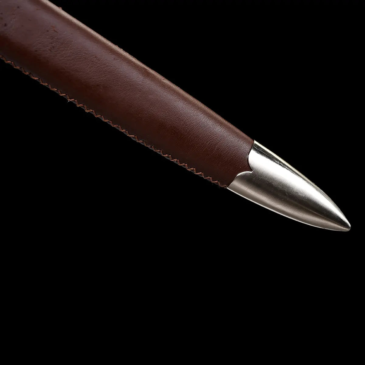 Gros plan du bout renforcé du fourreau de l’épée longue médiévale Vesper, en cuir brun lisse avec couture latérale visible et pointe métallique polie, présenté sur fond noir pour mettre en valeur les textures du cuir et de l’acier — fourreau cuir brun, longsword médiéval, finition premium.