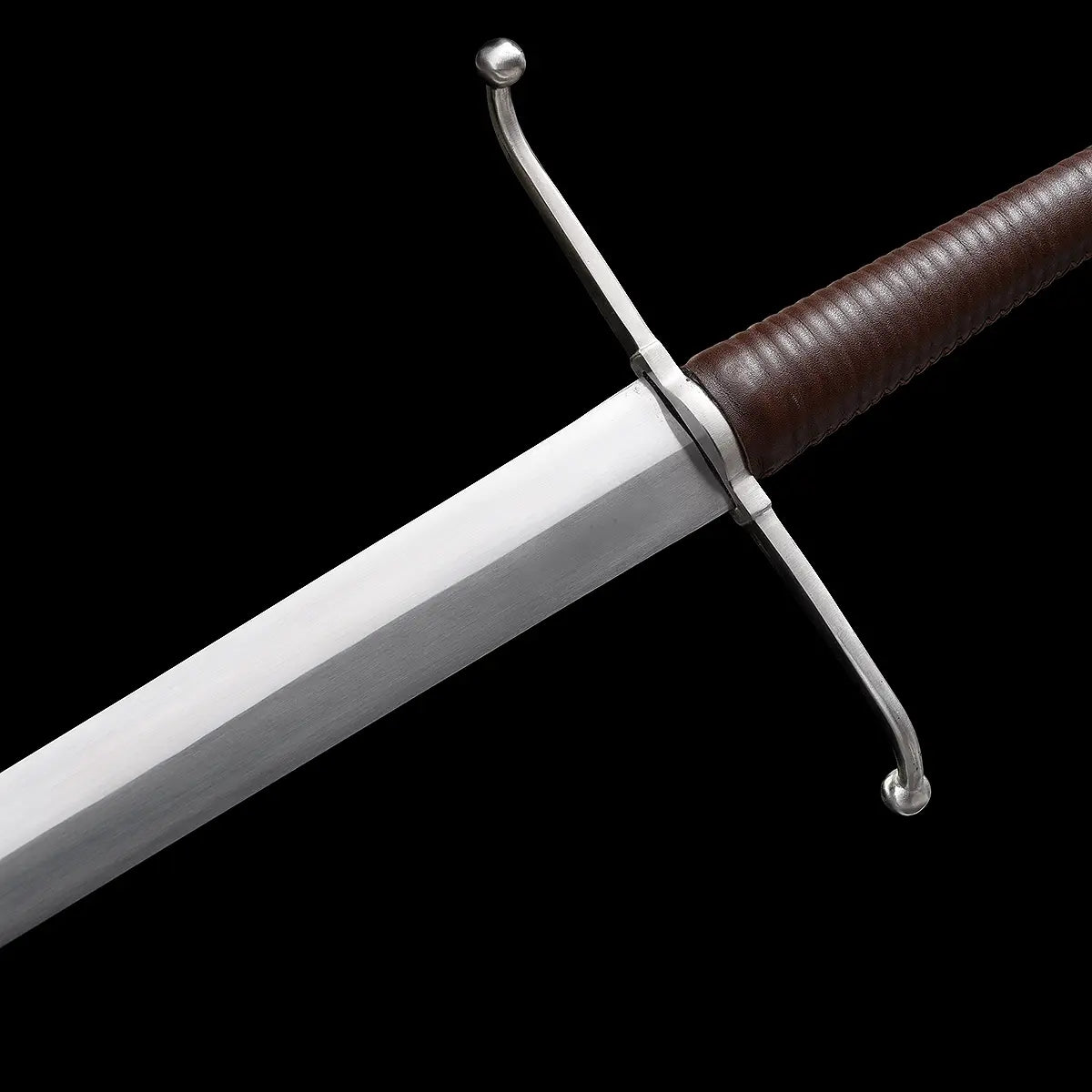 Détail de la garde en croix et de la poignée de l’épée longue Valmont, quillons incurvés en acier, poignée gainée de cuir brun nervuré, lame acier 1060 polie, fond noir studio