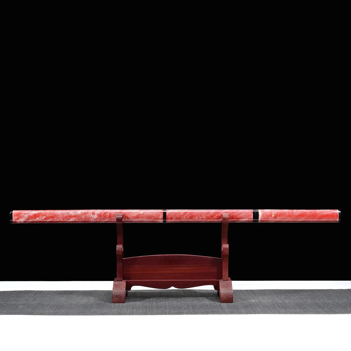 Épée chinoise Jian FEN LIN présentée dans son fourreau rose en peau de raie sur un support en bois, avec poignée assortie, finitions noires brillantes, fond noir et tapis gris en dessous.