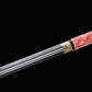 Épée chinoise Jian FEN LIN avec lame droite double tranchant partiellement sortie du fourreau rose en peau de raie, détail de la gorge centrale de la lame, garniture en laiton gravé et finition noire sur fond noir.