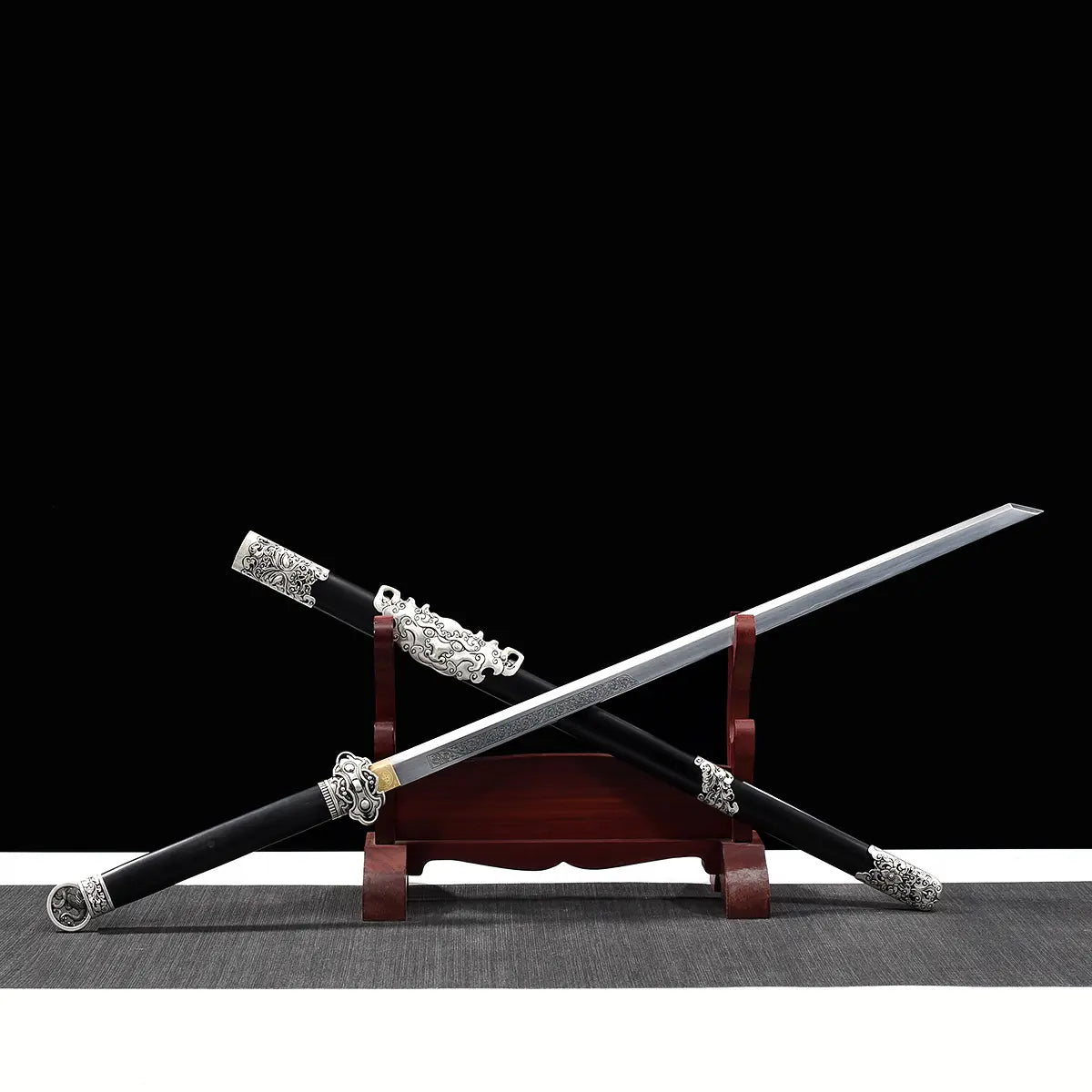 Épée chinoise Jian FENG YIN partiellement sortie de son fourreau noir, présentée en diagonale sur un support en bois rouge avec fond noir. La lame droite gravée, la garde argentée travaillée, le pommeau décoratif et les garnitures métalliques du fourreau mettent en valeur un Jian chinois artisanal de collection, adapté au Tai Chi, au Wushu et à la décoration.