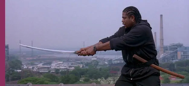 Side view of a Japanese shirasaya katana held with both hands by a man dressed in black, curved steel blade fully drawn from its wooden scabbard, light gray sky background with an industrial city landscape in the distance, natural outdoor lighting, minimalist wooden handle and saya with smooth finish, no guard visible, sharp tip and continuous curvature of the blade clearly defined
