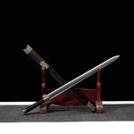Épée chinoise Jian HAN YUN photographiée en angle diagonal sur support en bois rouge, avec lame droite à pointe centrale, fourreau sombre en ébène, poignée noire, garde gravée et garnitures dorées sur fond noir.
