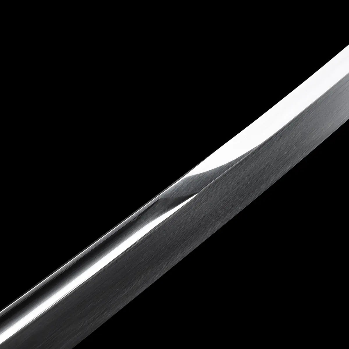 Détail rapproché de la lame du katana japonais artisanal Kazekiri montrant la géométrie unokubi-zukuri, amincissement progressif du dos de la lame avec transition visible, acier carbone 1060 à finition satinée et tranchant poli brillant, surface métallique texturée, fond noir uniforme mettant en valeur la forme et la ligne de la lame
