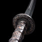 Gros plan du sabre chinois Dao KANGXI LONG avec garde ronde gravée, poignée noire texturée aux motifs métalliques sombres et lame courbe floutée en arrière-plan sur fond noir.