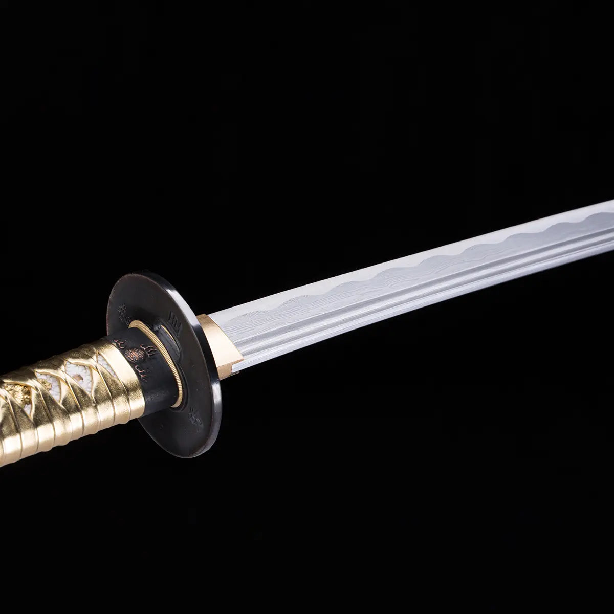Détail de la lame du katana japonais Toyotomi Hideyoshi en acier plié 880 couches avec hamon ondulé visible. Tsuba noire circulaire et tsuka doré mis en valeur sur fond noir studio Blade Bushido.