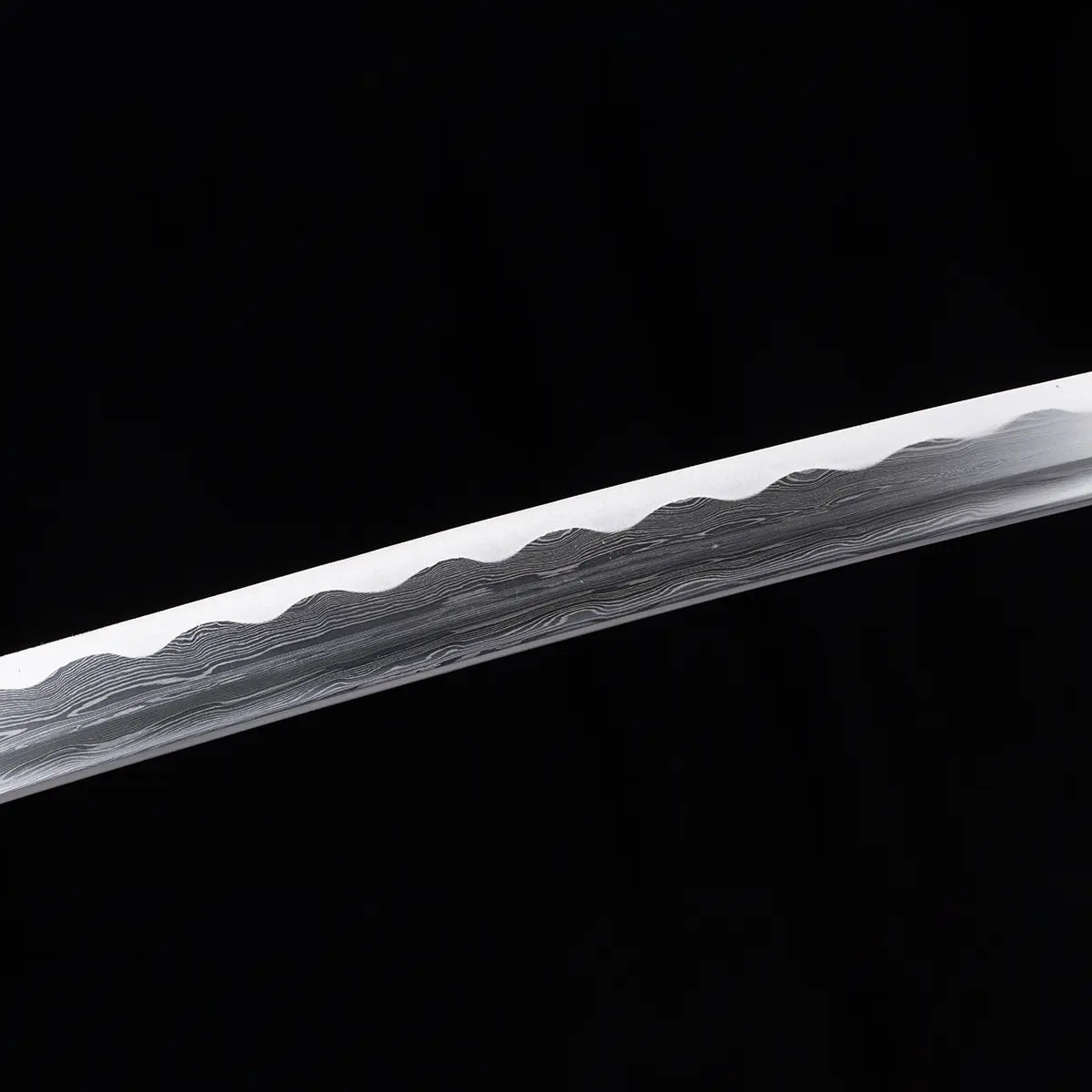 Gros plan sur la lame damassée du katana japonais Toyotomi Hideyoshi, montrant les 880 couches d’acier plié et le hamon ondulé distinctif, photographié sur fond noir studio Blade Bushido.