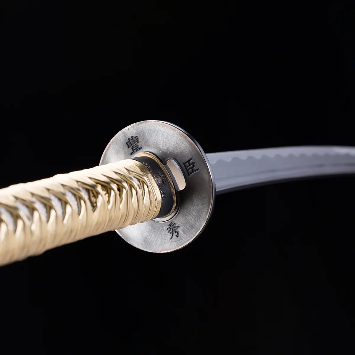 Vue rapprochée du katana japonais Toyotomi Hideyoshi montrant la tsuba métallique gravée de caractères japonais, le tsuka doré tressé et la lame en acier plié avec hamon ondulé, sur fond noir studio Blade Bushido.