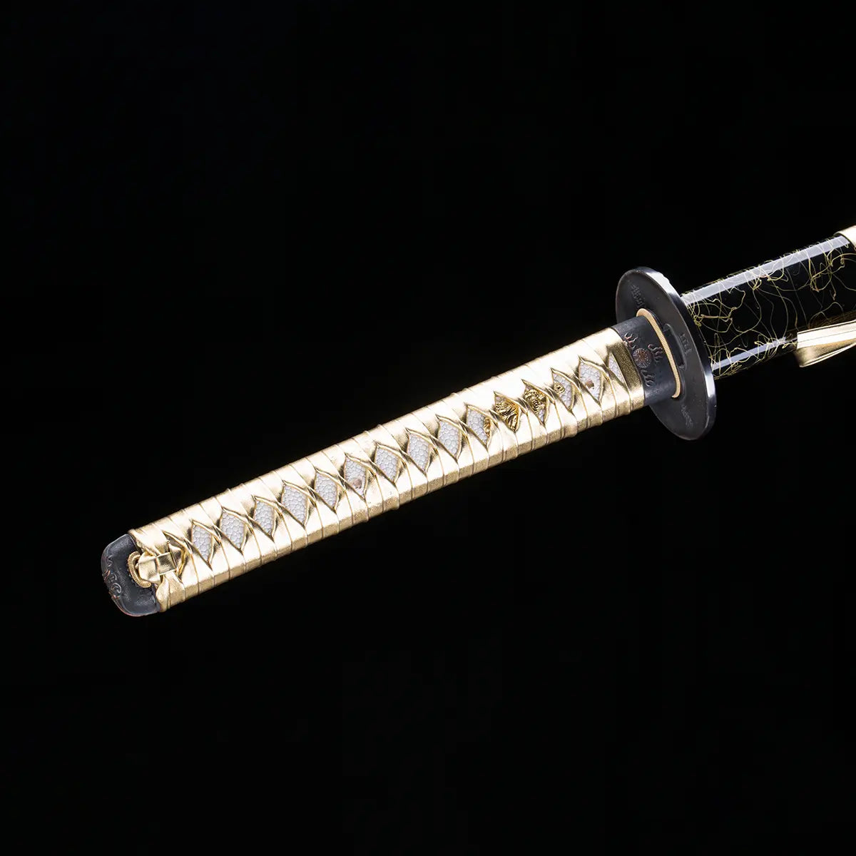 Détail du manche du katana japonais Toyotomi Hideyoshi en finition or et noir, tsuka tressé doré avec samegawa clair et garde noire, photographié sur fond noir studio pour Blade Bushido.
