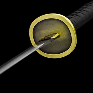 Vue détaillée de l’arrière de la garde du katana Aki Hayakawa Curse Blade inspiré de Chainsaw Man, photographiée sur fond noir uni. La tsuba circulaire dorée est visible côté intérieur, avec une surface mate et un pourtour lisse. Le habaki doré texturé entoure la base de la lame en acier carbone poli, tandis que le manche recouvert de tsuka-ito noir apparaît partiellement à l’arrière. Aucun fourreau ni support présent, mise en valeur de l’assemblage et des finitions, adaptée à une
