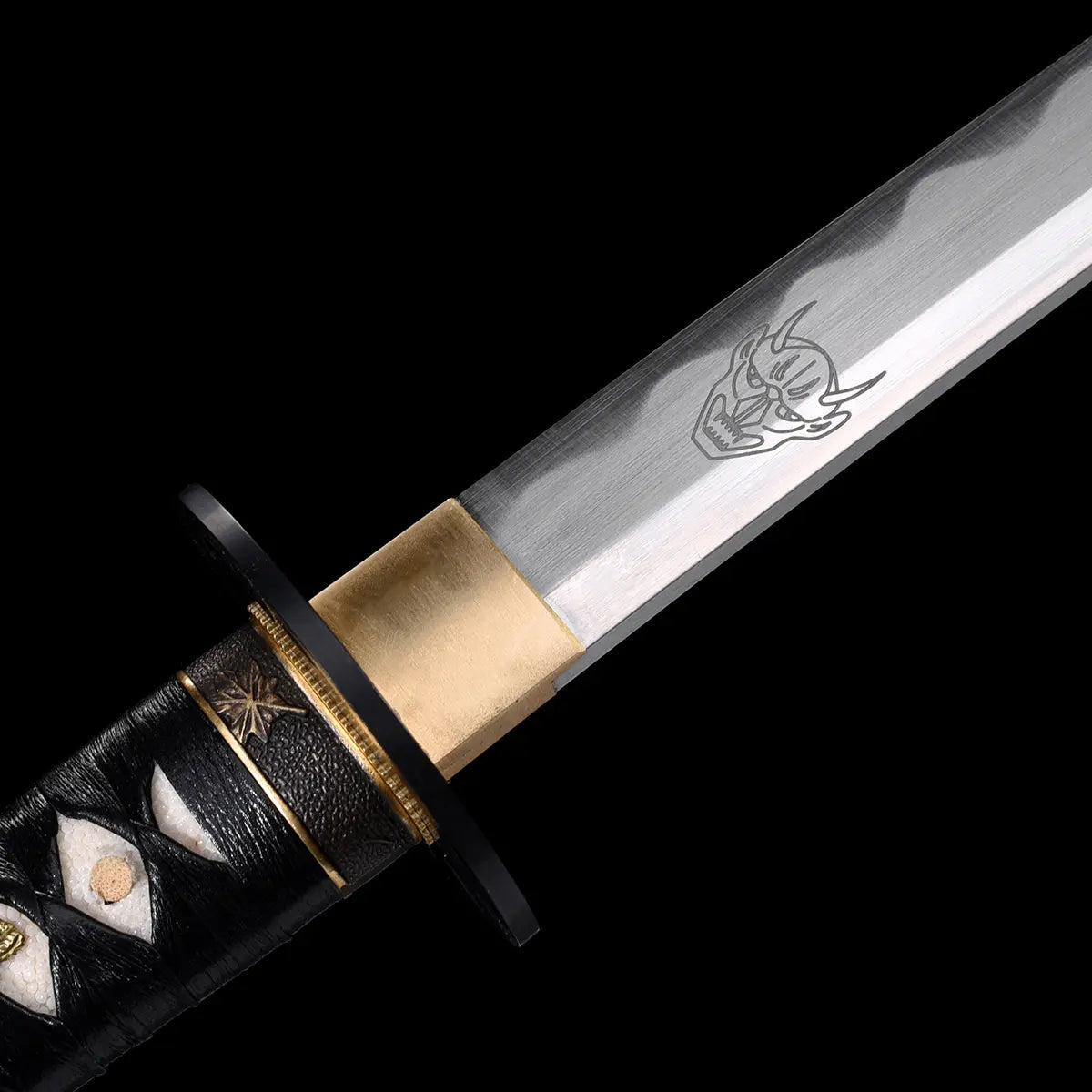 Gros plan sur la garde et la base de la lame du katana de Bill dans Kill Bill, acier carbone 1045 avec gravure démon, tsuba noir et manche en cuir noir avec samegawa blanc, fond noir minimaliste.