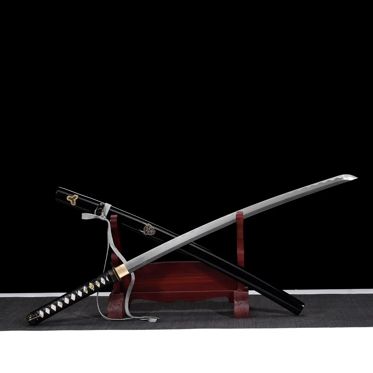 Katana de Bill dans Kill Bill dégainé de son saya noir laqué orné, lame en acier carbone 1045 hamon ondulé, manche tsuka noir tressé avec samegawa blanc, présenté sur support en bois rouge, fond noir minimaliste.