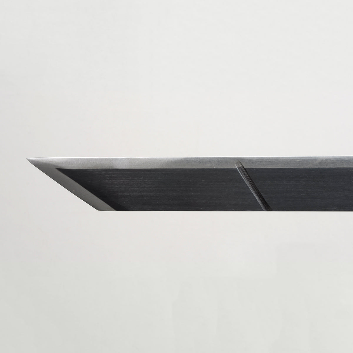 Gros plan de la pointe du katana de Eren Jäger “Lame anti-Titans”, réplique Attack on Titan en acier carbone noir, lame rectangulaire avec arêtes métalliques argentées, photographiée sur fond gris clair minimaliste.