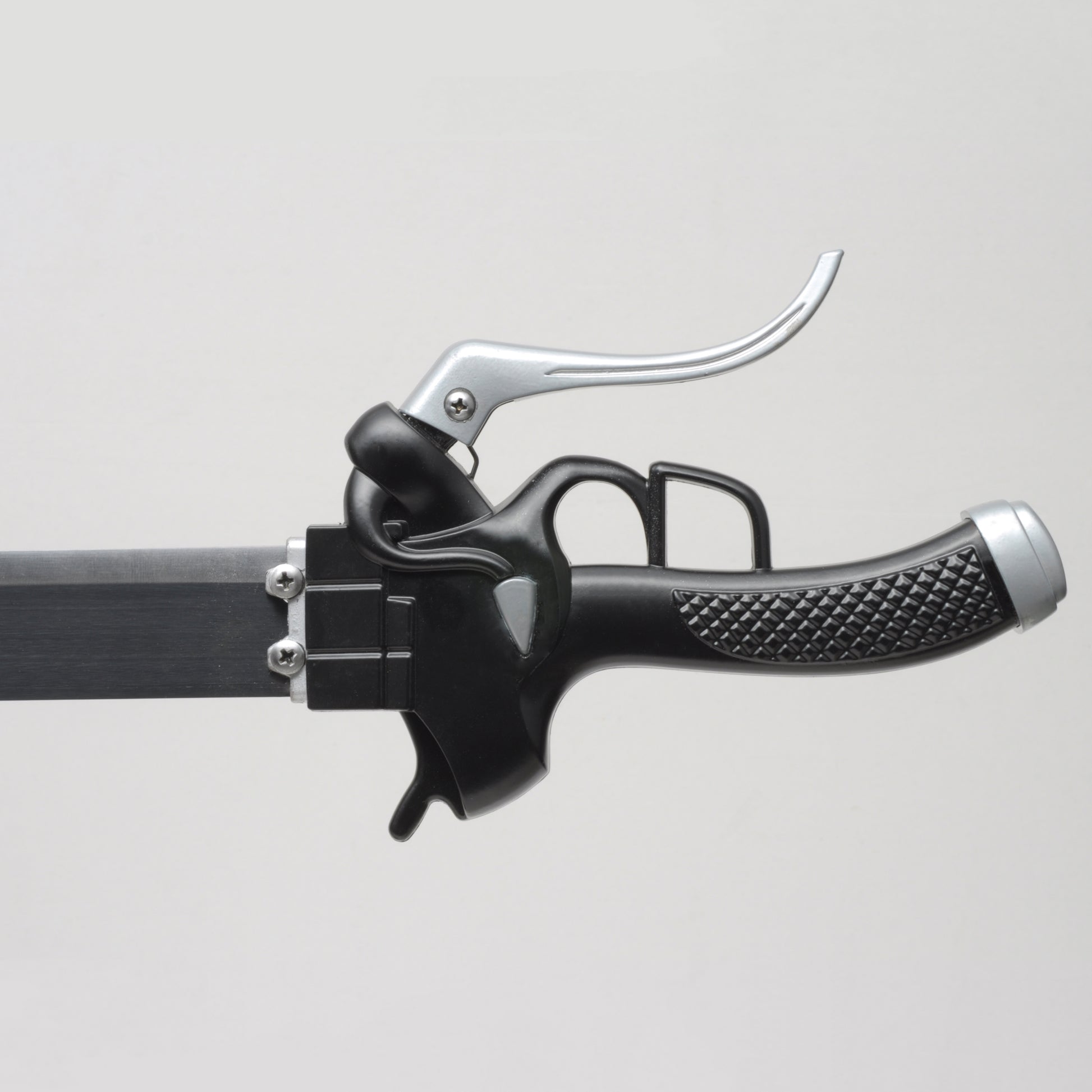 Gros plan de la poignée noire texturée du katana de Eren Jäger “Lame anti-Titans”, réplique Attack on Titan en acier carbone, garde métallique argentée avec levier caractéristique, photographié sur fond gris clair.