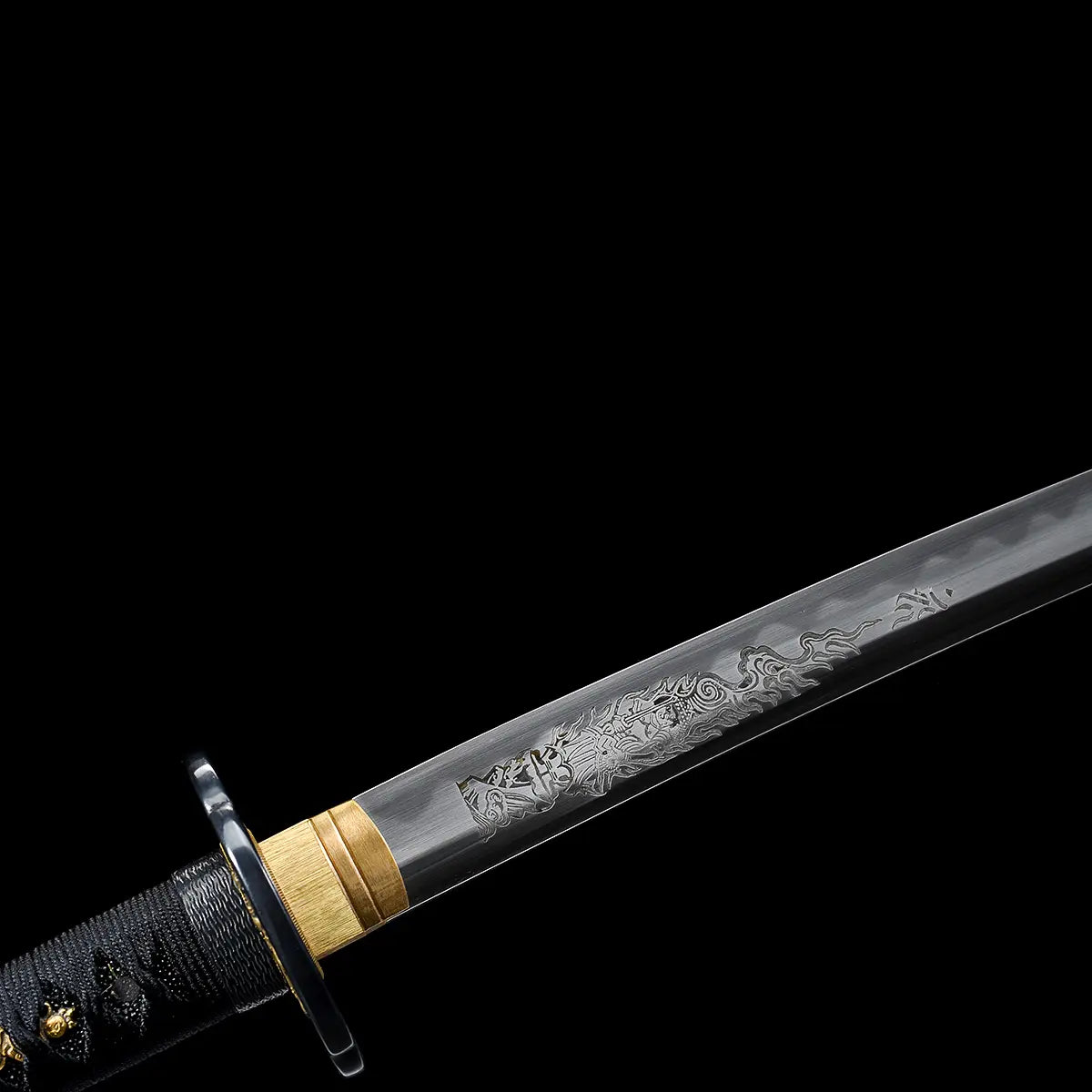 Close-up of a Japanese katana blade against a deep black background, polished steel surface featuring an engraved Fudo Myoo figure near the base of the blade, gold-colored brass habaki fitted tightly against the blade, round black tsuba partially visible, black handle wrapped in black cord over ray skin, fine engraving lines and steel texture clearly visible, focus on blade craftsmanship and spiritual engraving details.
